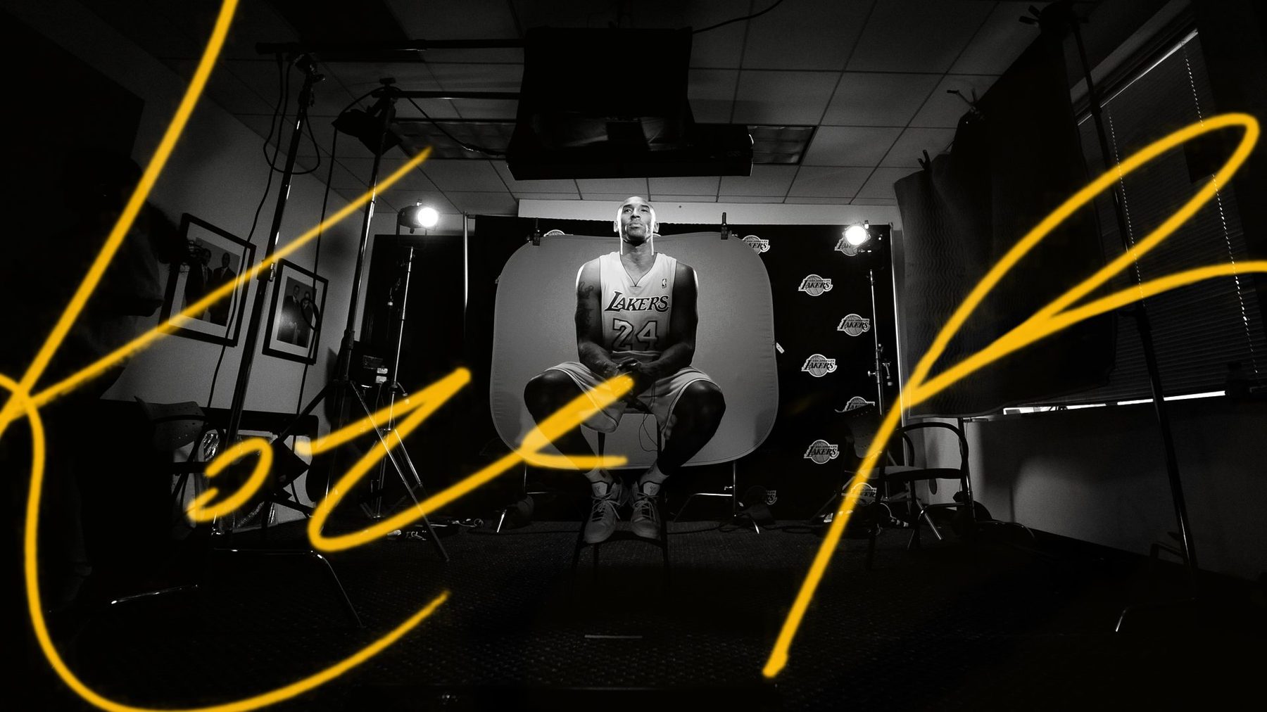 Kobe Bryant seated on a studio set, overlaid with his signature in Lakers gold